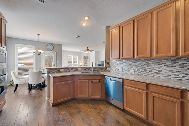 Kitchen with wood finished floors, backsplash, appliances with stainless steel finishes, a sink, and brown cabinets | Image 13