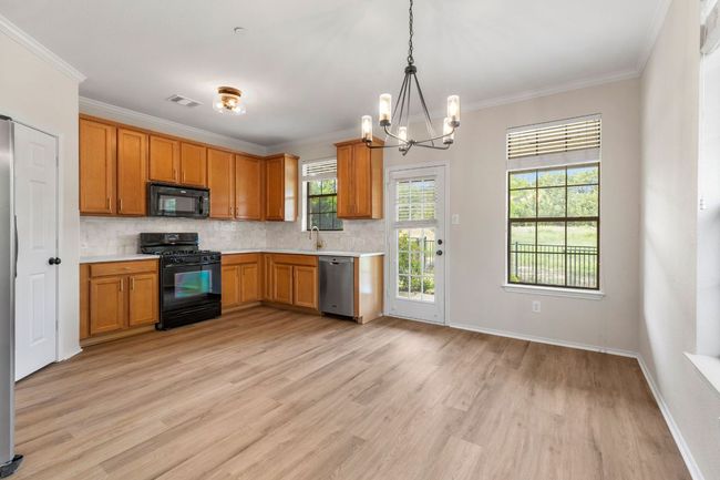 Kitchen with light countertops, light wood-type flooring, decorative backsplash, black appliances, and a chandelier | Image 12