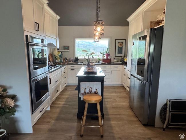 Kitchen featuring appliances with stainless steel finishes, dark countertops, white cabinets, and hanging light fixtures | Image 5