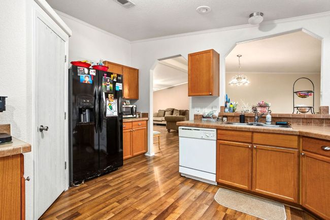 Kitchen featuring black fridge with ice dispenser, ornamental molding, a sink, white dishwasher, and wood finished vinyl floors | Image 16