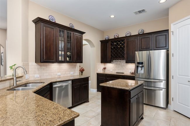 Kitchen featuring appliances with stainless steel finishes, arched walkways, dark brown cabinetry, light stone counters, and tasteful backsplash | Image 18