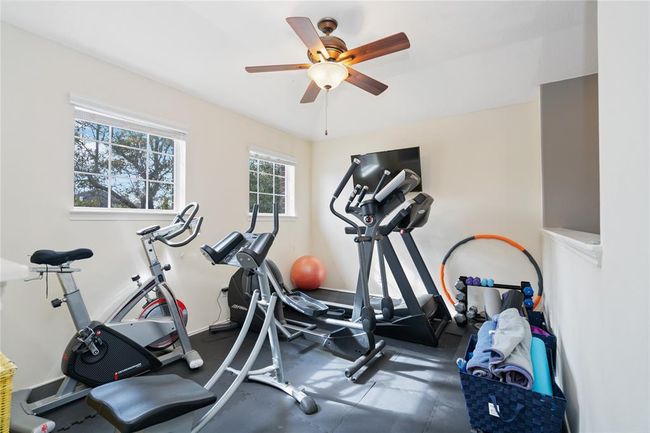 This home features a bright and functional personal gym with large windows, equipped with a treadmill, exercise bike, and fitness accessories, under a ceiling fan for ventilation. | Image 42