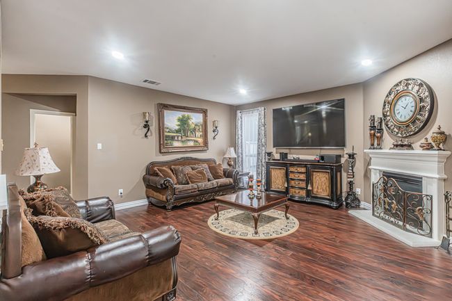 Living area with a fireplace with raised hearth, wood finished floors, and recessed lighting | Image 11