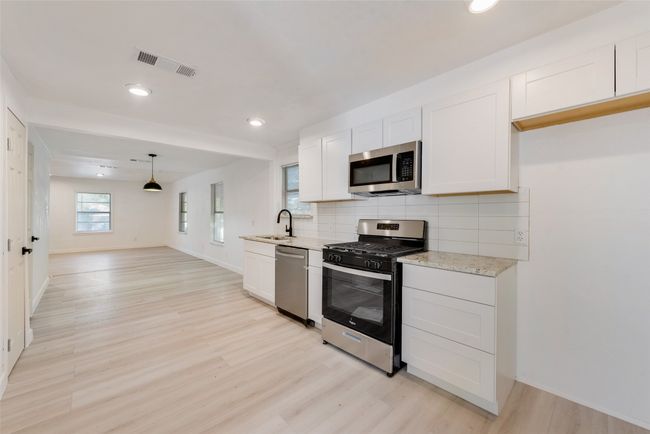 Kitchen with light wood finished floors, stainless steel appliances, a sink, visible vents, and decorative backsplash | Image 13