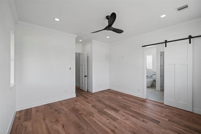 Spacious primary bedroom featuring elegant LVP floors, modern ceiling fan, and convenient ensuite access with a stylish sliding barn door. | Image 24