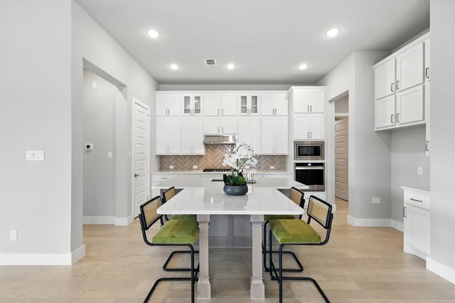 Kitchen with appliances with stainless steel finishes, under cabinet range hood, a kitchen bar, tasteful backsplash, and an island with sink | Image 5