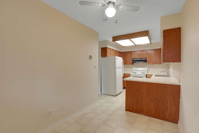 Kitchen with white appliances, extractor fan, brown cabinets, a peninsula, and light countertops | Image 17