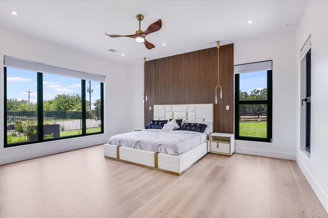Primary Bedroom on main floor with large windows, light wood-style flooring, wood accent wall, custom sconce lighting as well as recessed lighting, and ceiling fan | Image 24