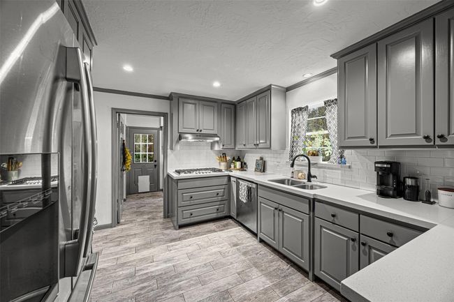 This kitchen features sleek gray cabinetry, modern stainless steel appliances, and a stylish tile floor. It has ample counter space and a bright, welcoming atmosphere with natural light from a window above the sink. | Image 14