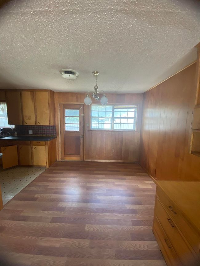 Kitchen with wood walls, light wood-style flooring, a textured ceiling, and dark countertops | Image 5