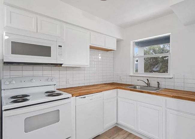 Kitchen featuring white appliances, wooden counters, backsplash, and white cabinets | Image 14