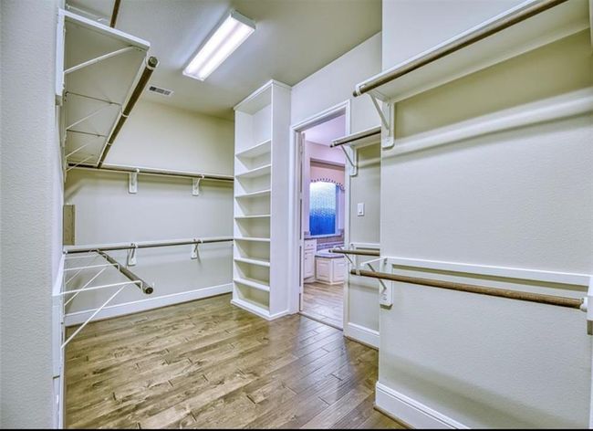 This photo showcases a spacious walk-in closet with ample shelving and hanging space. It features hardwood flooring and leads into a well-lit bathroom with a large vanity. | Image 32