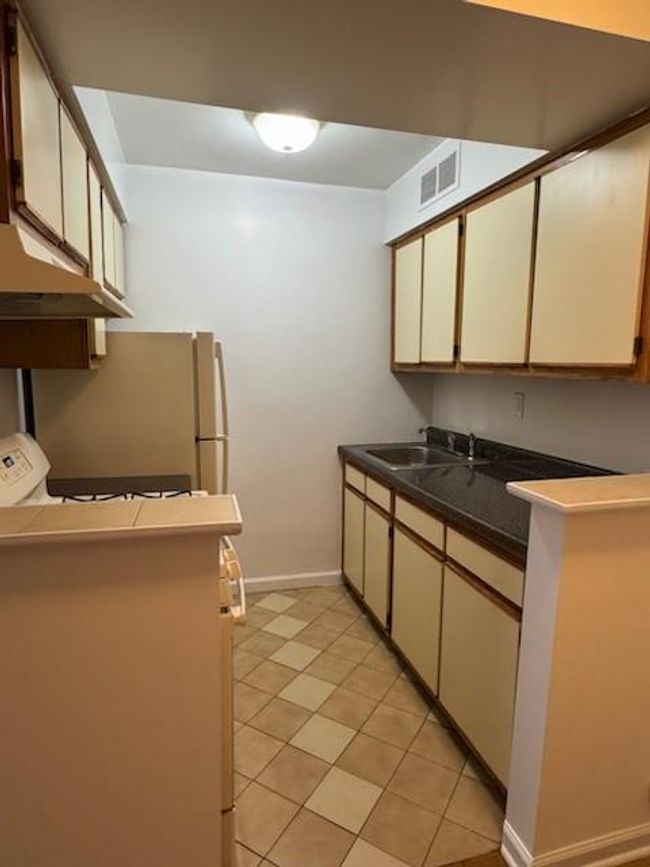 Kitchen featuring baseboards, visible vents, dark countertops, a sink, and exhaust hood | Image 5