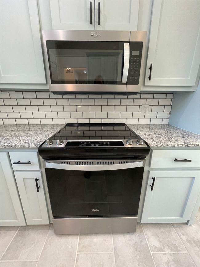 Interior details featuring backsplash, electric range oven, light stone countertops, and white cabinets | Image 21