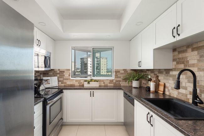 Kitchen with stainless steel appliances, a raised ceiling, dark stone countertops, white cabinetry, and backsplash | Image 20