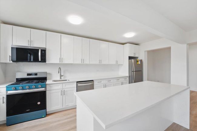 Kitchen featuring light wood finished floors, stainless steel appliances, white cabinets, a sink, and light countertops | Image 7
