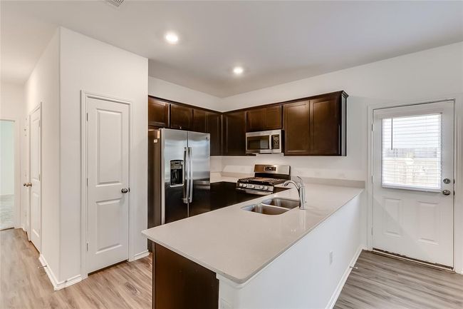 Kitchen with stainless steel appliances, a sink, light wood-type flooring, dark brown cabinets, and light countertops | Image 13