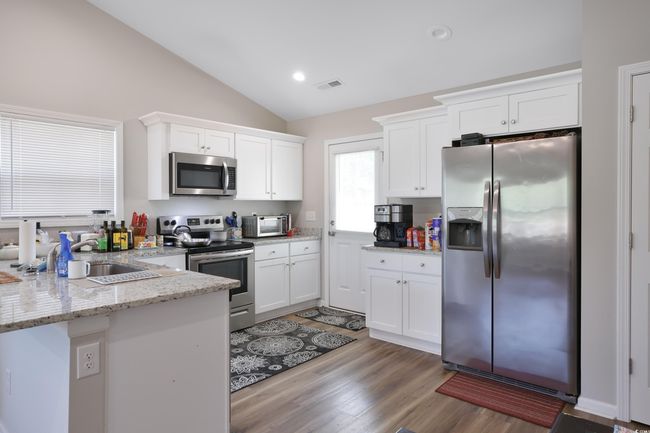 Kitchen featuring stainless steel appliances, lofted ceiling, white cabinetry, light stone counters, and light wood-type flooring | Image 13