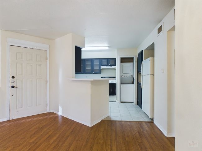 Kitchen featuring electric stove, freestanding refrigerator, under cabinet range hood, stacked washer and clothes dryer, and a peninsula | Image 5