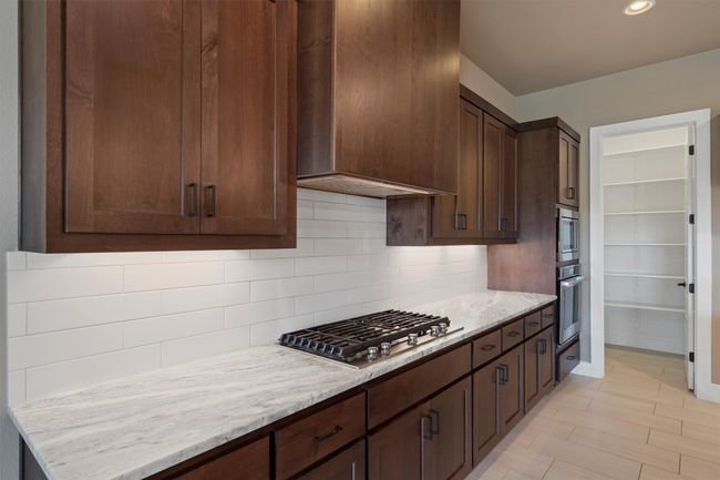 Kitchen with stainless steel appliances, tasteful backsplash, custom exhaust hood, light stone counters, and dark brown cabinetry | Image 10