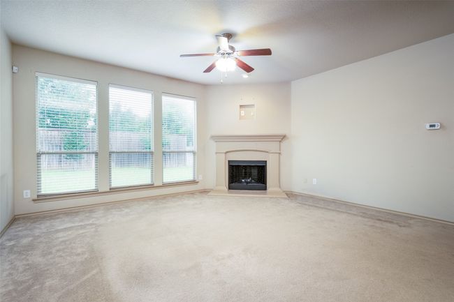 Unfurnished living room featuring a ceiling fan, carpet floors, and a fireplace with raised hearth | Image 7