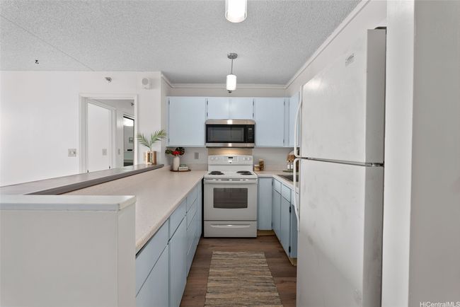 This galley-style kitchen offers generous counter space and ample cabinetry, making the layout ideal for everyday cooking. Thoughtful touches like pendant lighting and a peek-through opening to the living room keep the space light and connected. | Image 4