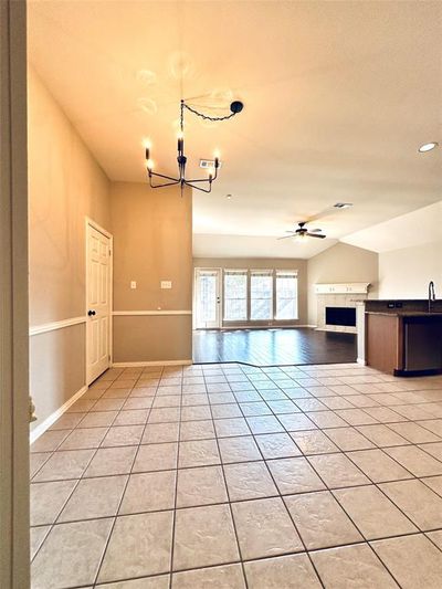 Unfurnished living room featuring ceiling fan with notable chandelier, lofted ceiling, light tile patterned flooring, and a tiled fireplace | Image 3