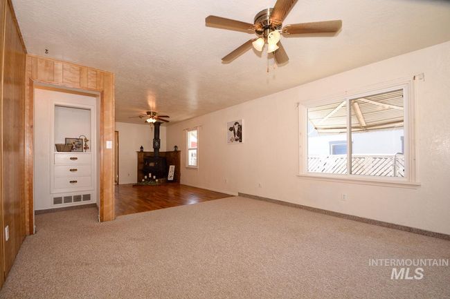 Unfurnished living room with carpet flooring, a wood stove, a ceiling fan, and a textured ceiling | Image 16