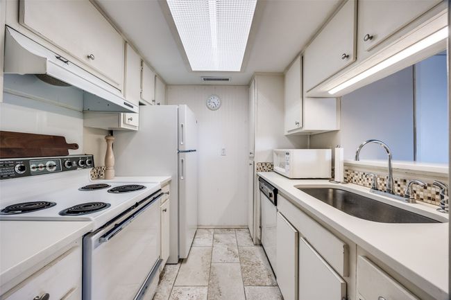 Kitchen with white appliances, a stainless steel sink, white cabinetry, tile floors, and light stone countertops | Image 8