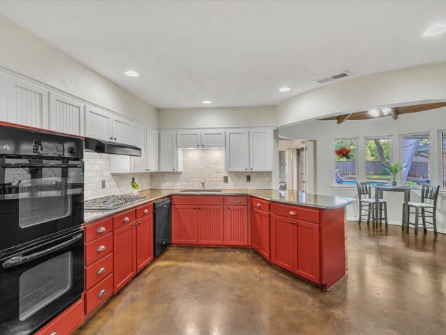 Kitchen with black appliances, concrete flooring, backsplash, a peninsula, and recessed lighting | Image 14