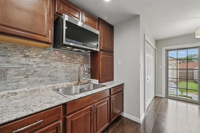 Kitchen with stainless steel microwave, a sink, dark wood finished floors, decorative backsplash, and baseboards | Image 4