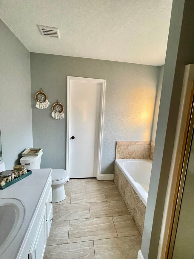 Bathroom with a textured ceiling, vanity, toilet, and a relaxing tiled tub | Image 13