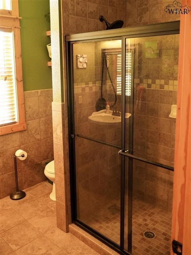 Bathroom featuring toilet, sink, tile walls, and a shower with door | Image 8