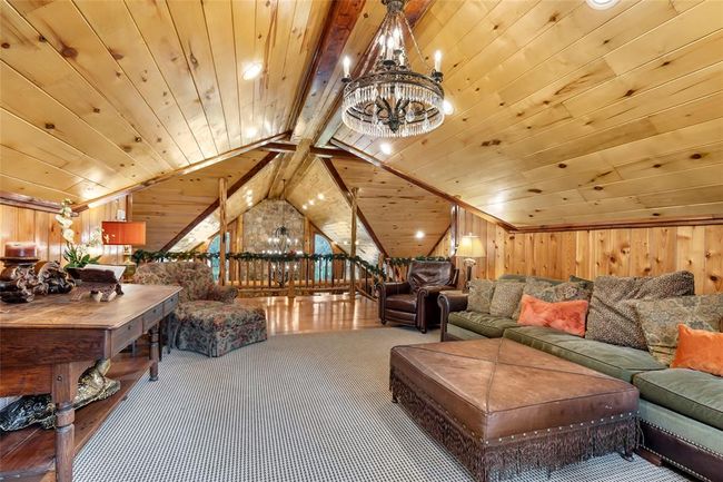 This cozy loft features rich wood paneling and a vaulted ceiling, creating a warm, rustic ambiance. It includes a comfortable seating area with a large sectional sofa, a stylish chandelier, and a mix of plush and leather chairs, perfect for relaxation or entertaining. | Image 38