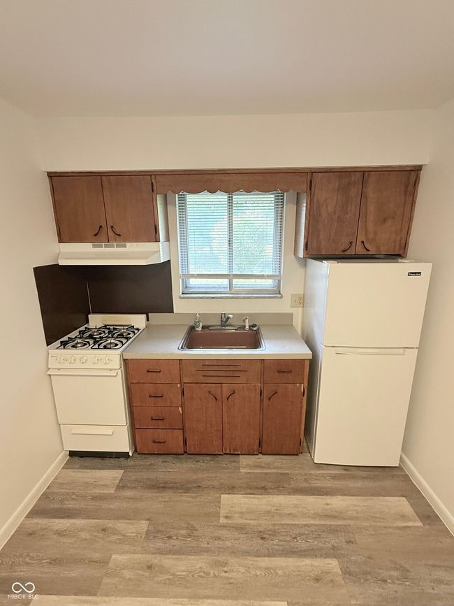 kitchen featuring white appliances, light wood-style flooring, light countertops, and under cabinet range hood | Image 6