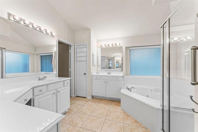 The spacious primary bath offers a spa-like retreat with a deep soaking tub, separate glass-enclosed shower, and expansive vanity with dual sinks and a makeup area. | Image 27