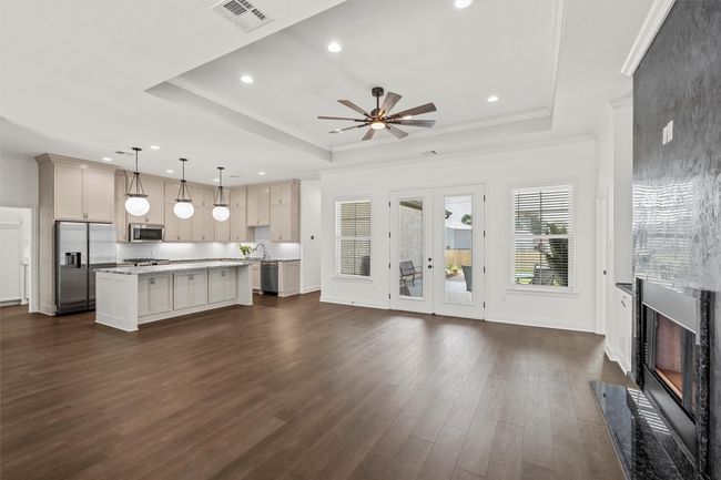 Unfurnished living room with a high end fireplace, a ceiling fan, dark wood-style flooring, a raised ceiling, and crown molding | Image 7