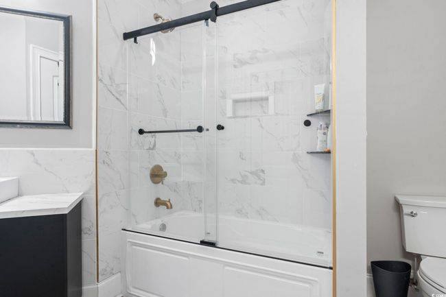 Full bathroom featuring toilet, shower / bath combination with glass door, and tile walls | Image 30