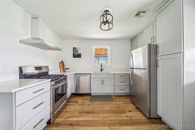 Kitchen featuring stainless steel appliances, wall chimney range hood, a sink, light wood finished floors, and light countertops | Image 19