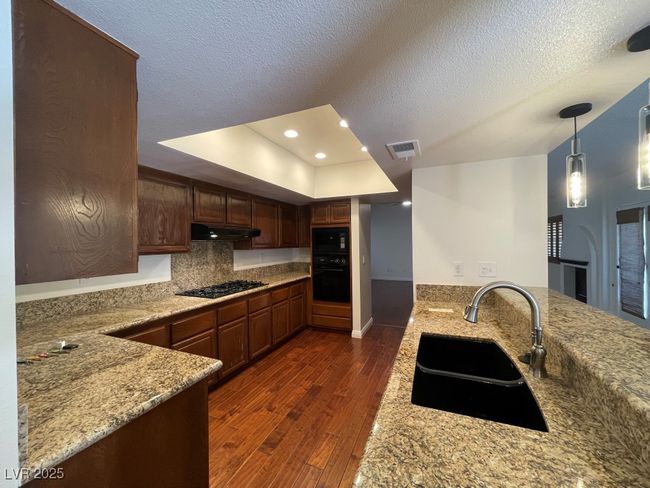 Kitchen with black appliances, a peninsula, dark wood-type flooring, light stone countertops, and recessed lighting | Image 5