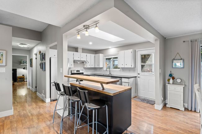 Kitchen featuring light wood-style flooring, white cabinets, under cabinet range hood, a sink, and butcher block countertops | Image 5
