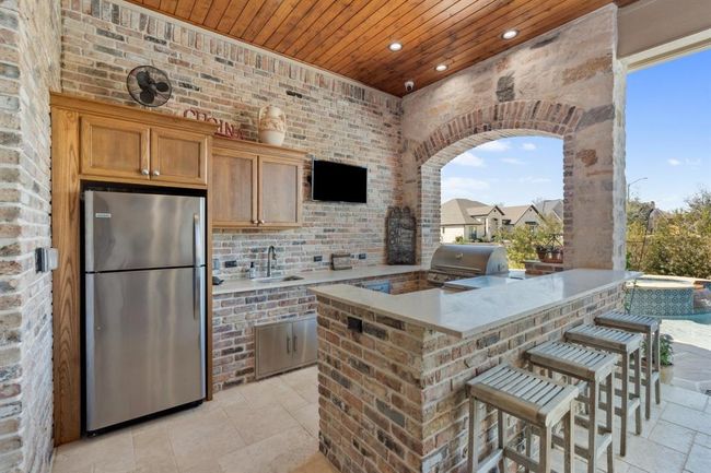 Custom wall-mounted stained white oak cabinets with stainless lower cabinets built in a wooden frame clad in Old Chicago Brick, including a raised barthat seats four. The countertops are leathered Taj Mahal quartzite. Theappliances include a 34" Blaze Gas Grill, a 30" Blaze Griddle, a stainless steel sink and faucet, and a full-sized Frigidaire stainless refrigerator. | Image 37