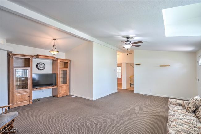 Unfurnished living room featuring carpet floors, ceiling fan, baseboards, vaulted ceiling, and a skylight | Image 7