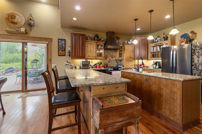 Kitchen featuring custom exhaust hood, a sink, a peninsula, hardwood / wood-style floors, and a center island with sink | Image 17
