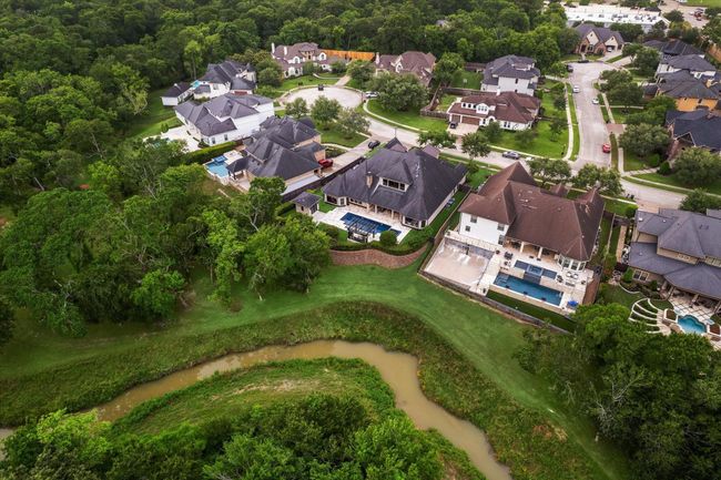 This aerial perspective highlights the home’s premium location at the curve of a tranquil cul-de-sac, backing to a lush greenbelt and gently winding creek for added serenity and privacy. The elevated lot and gracefully terraced landscaping create a distinct sense of space and seclusion, while still being seamlessly integrated into a desirable, well-established neighborhood. A true sanctuary with natural beauty just steps beyond your backyard. | Image 50