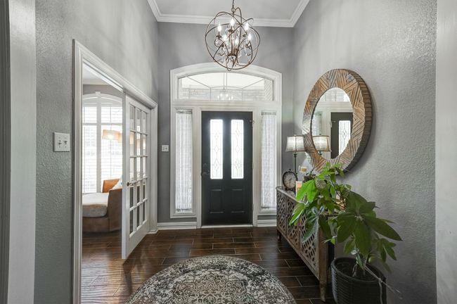 Foyer entrance featuring baseboards, a chandelier, a textured wall, crown molding, and wood tiled floor | Image 6