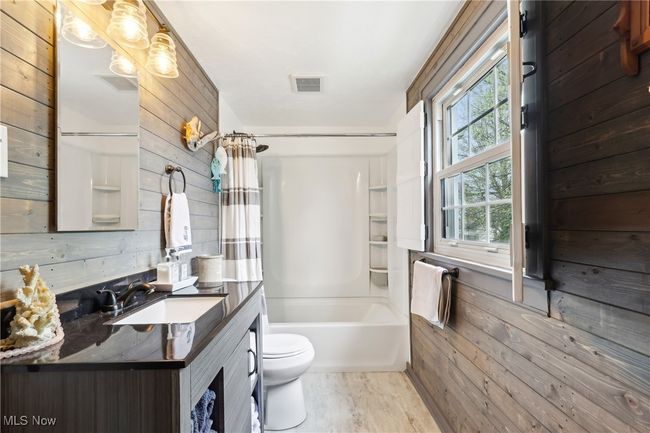 Bathroom featuring toilet, visible vents, shower / tub combo with curtain, wooden walls, and vanity | Image 23