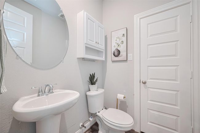 This is a compact, modern bathroom featuring a pedestal sink, a round mirror, a toilet and a closet for extra storage. | Image 23