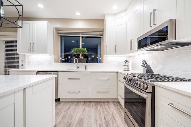 Kitchen with stainless steel appliances, backsplash, white cabinetry, light stone countertops, and light vinyl plank flooring | Image 7
