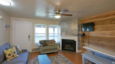 Living room with ceiling fan, wood walls, a textured ceiling, a baseboard heating unit, and hardwood / wood-style floors | Image 1